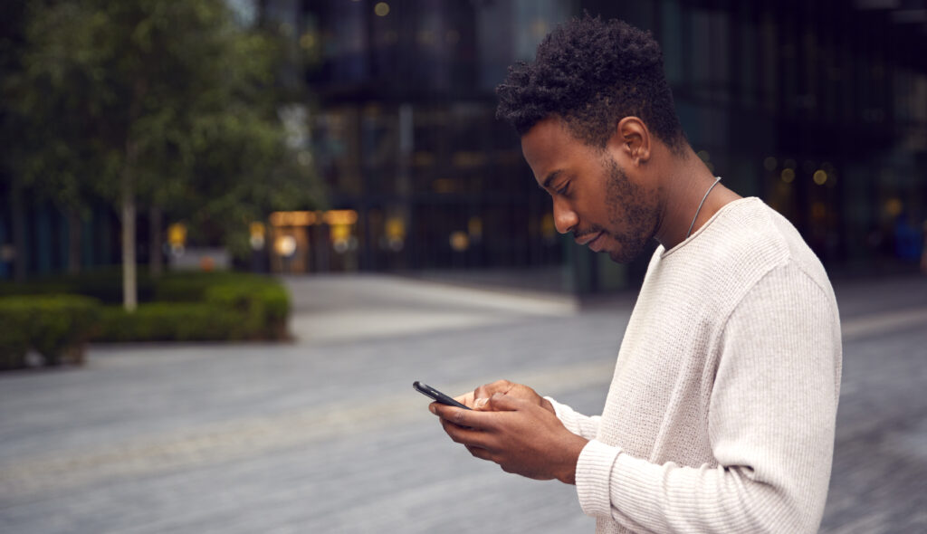 Male Vlogger Or Social Influencer In City Using Mobile Phone On Street To Post To Social Media